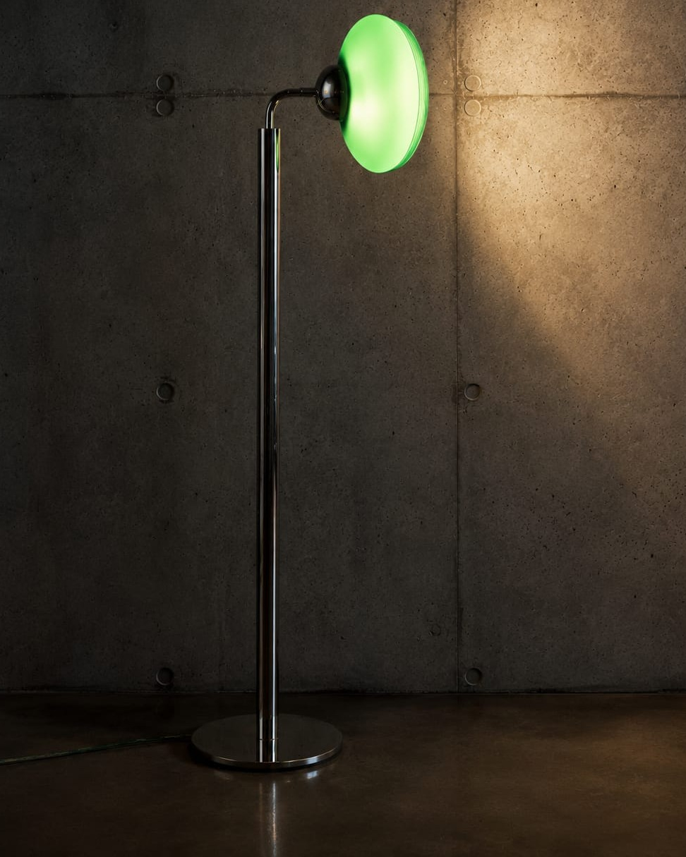 No. 009, Jade, a tall floor lamp with a green glowing oval shade, narrow reflective stem, round base, and visible dark cable.
